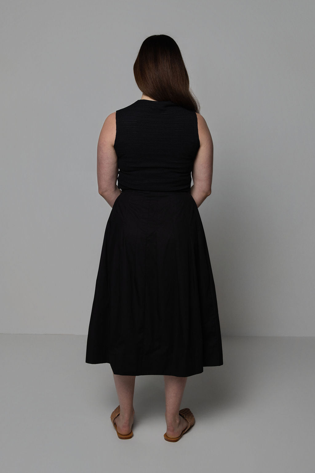 Woman wearing a black sleeveless top and black skirt against a plain background
