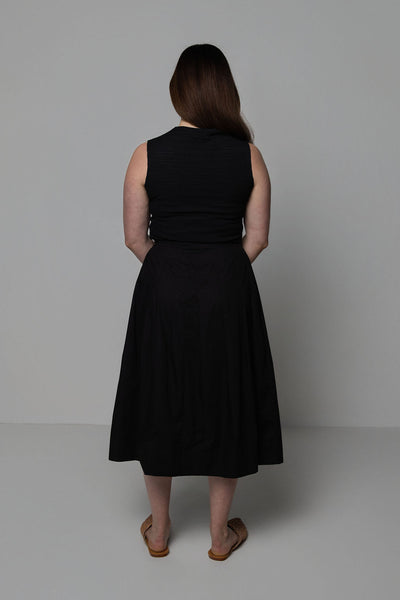 Woman wearing a black sleeveless top and black skirt against a plain background