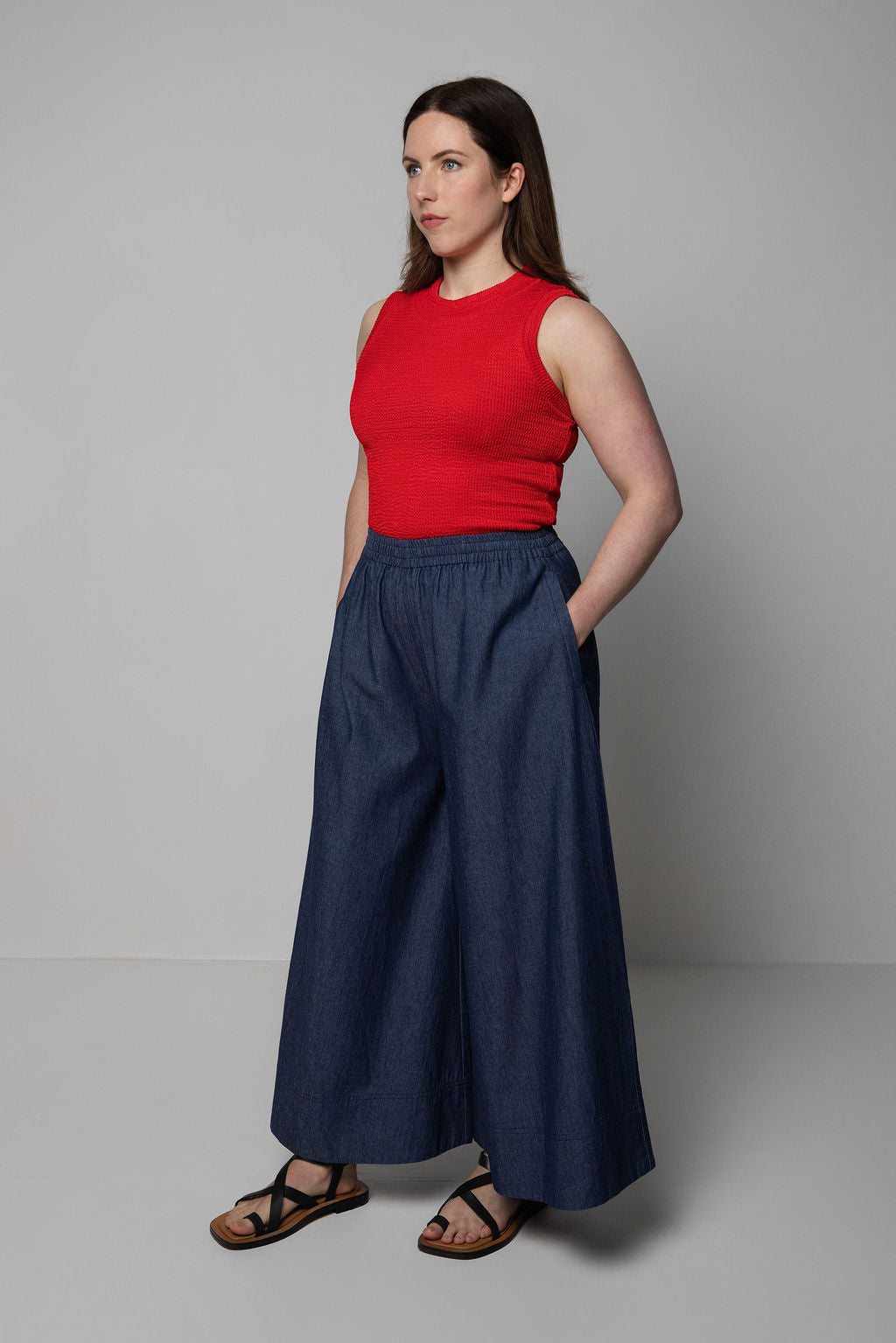 Woman wearing a red top and navy wide-leg pants against a gray background