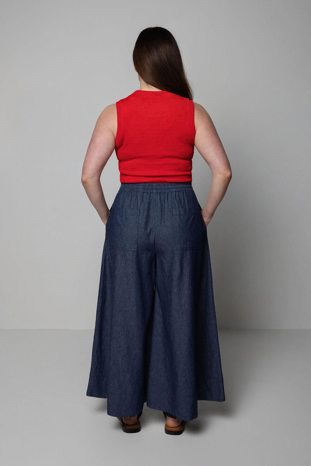 Person wearing a red top and blue wide leg pants against a plain background