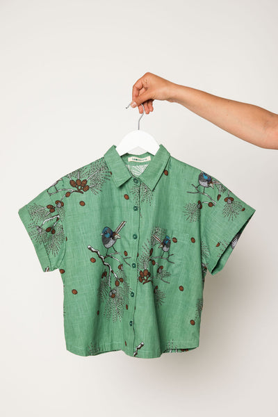 Green shirt with bird pattern on a hanger against a white background