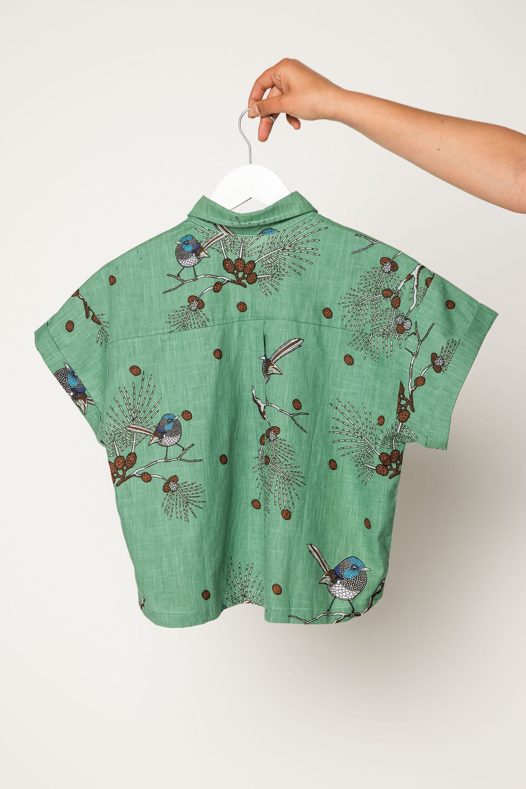 Green shirt with bird pattern on a hanger against a white background