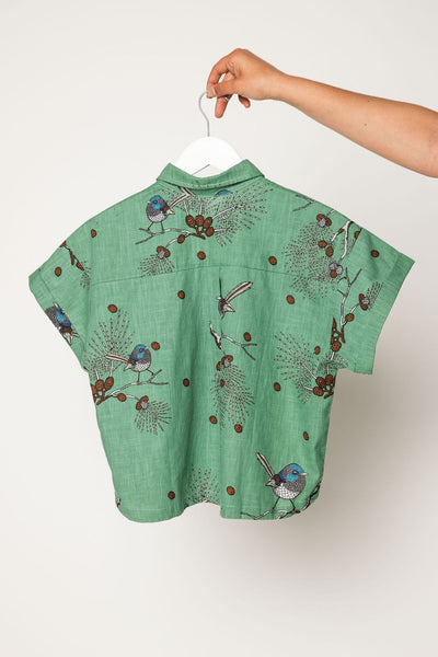Green shirt with bird pattern on a hanger against a white background