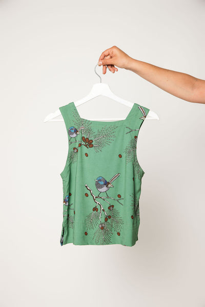 Green sleeveless top with bird and floral design on a white hanger against a white background