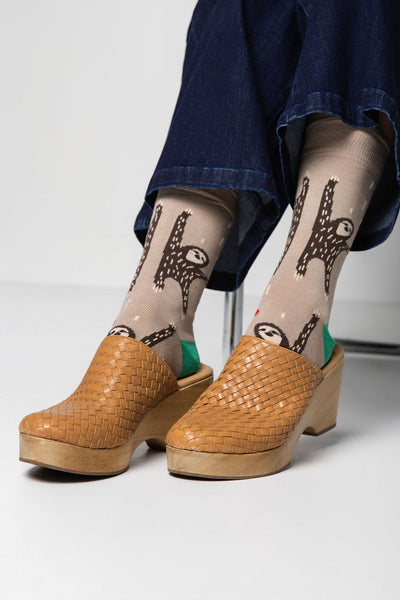 Person wearing beige socks with animal patterns and brown clogs on a light background