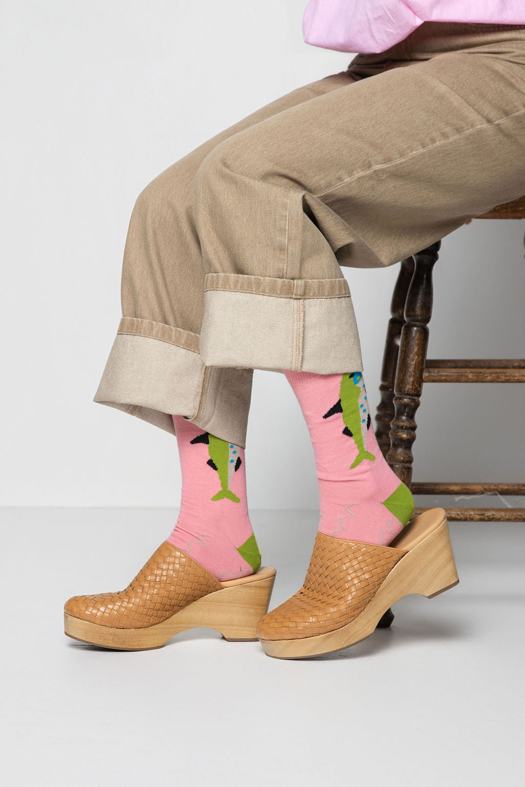Person wearing pink socks with green accents and brown clogs on a light gray background