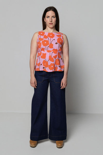 Woman wearing a sleeveless top with orange floral pattern and dark blue pants on a plain background