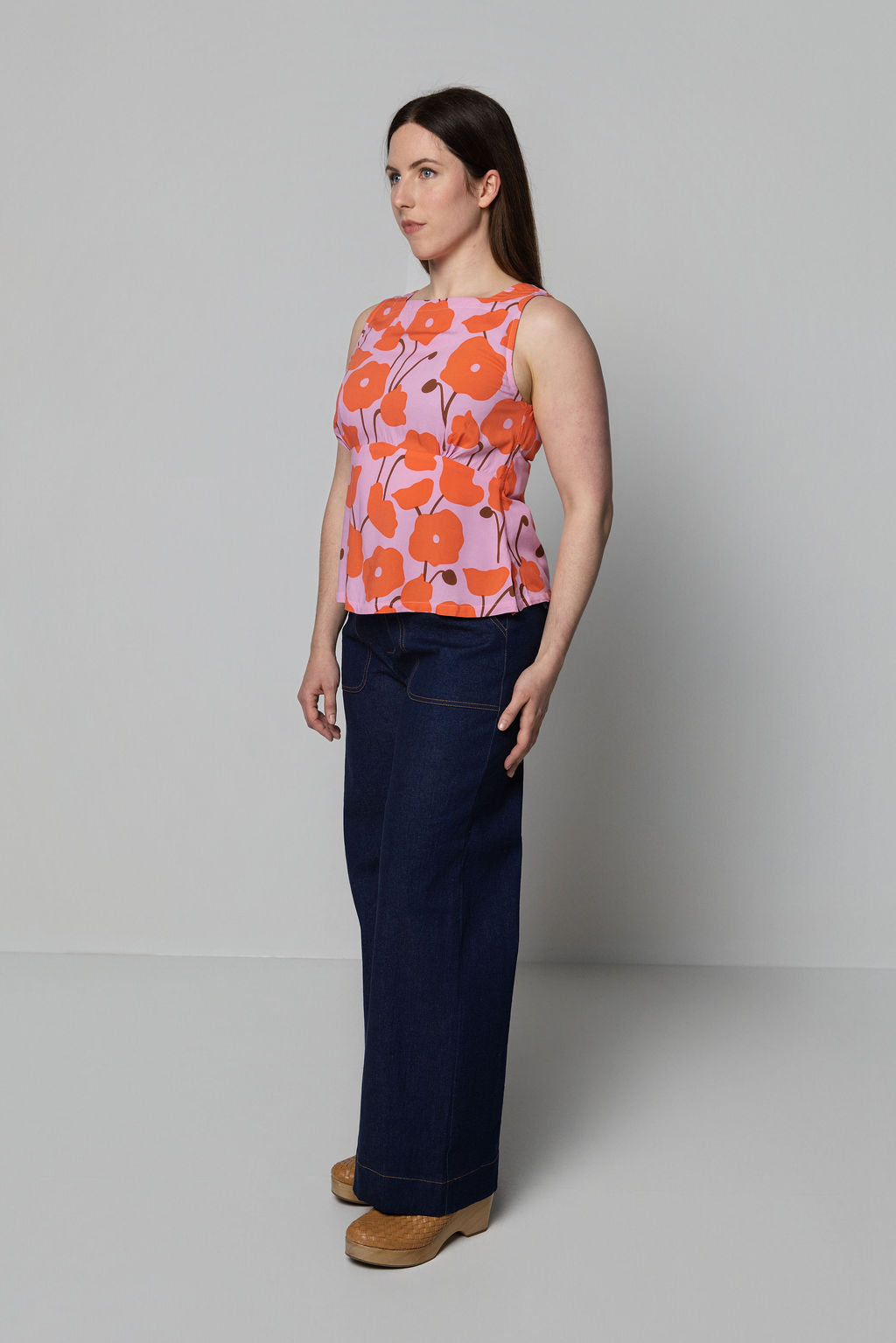 Woman wearing a sleeveless floral top and dark pants against a plain background