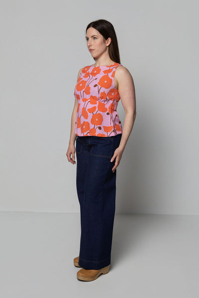 Woman wearing a sleeveless floral top and dark pants against a plain background
