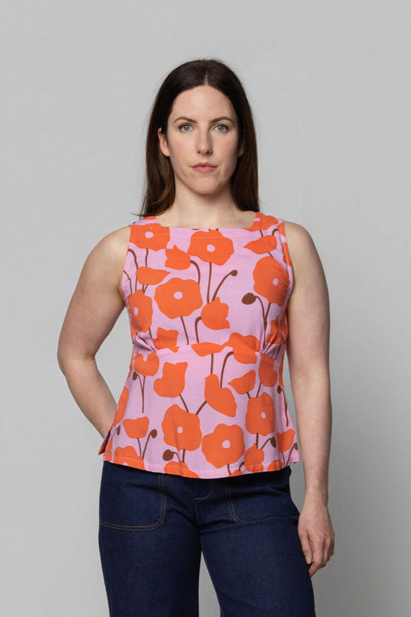 Woman wearing a sleeveless top with orange floral pattern on a plain background