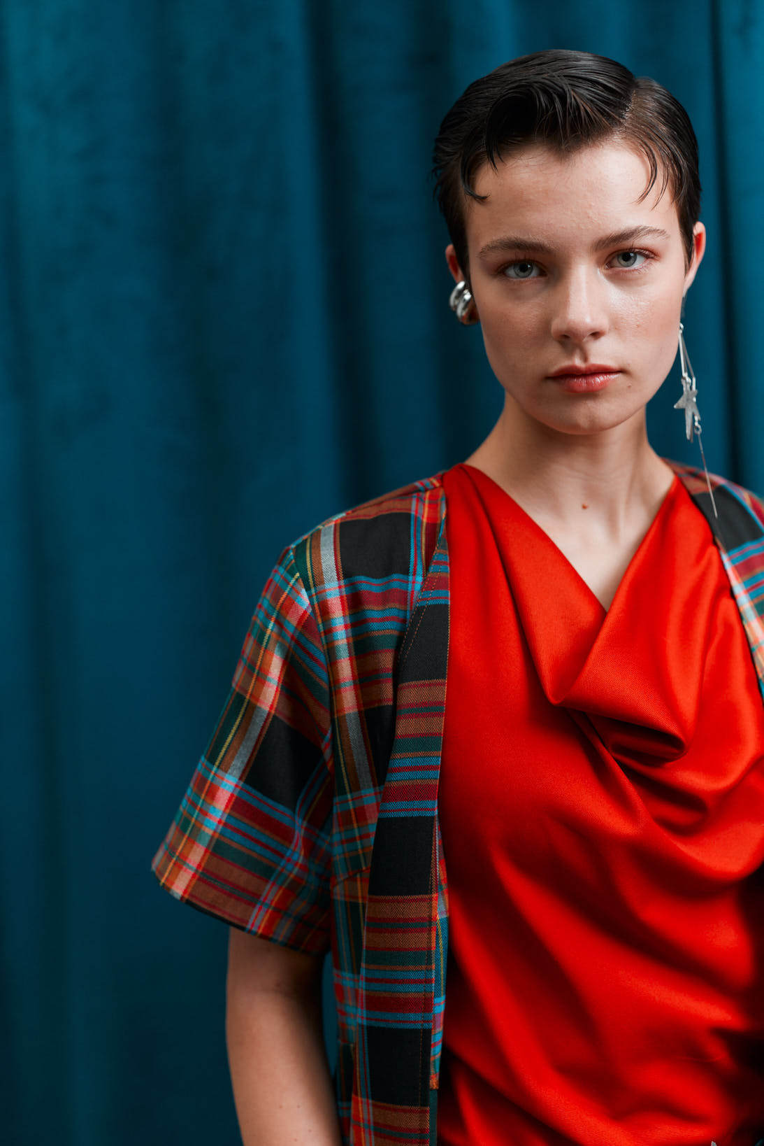 Woman wearing a red top and plaid shirt against a blue curtain