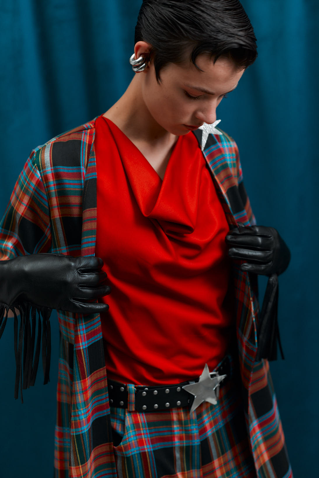 Person wearing a red top, plaid open shirt and matching pants, against a blue background