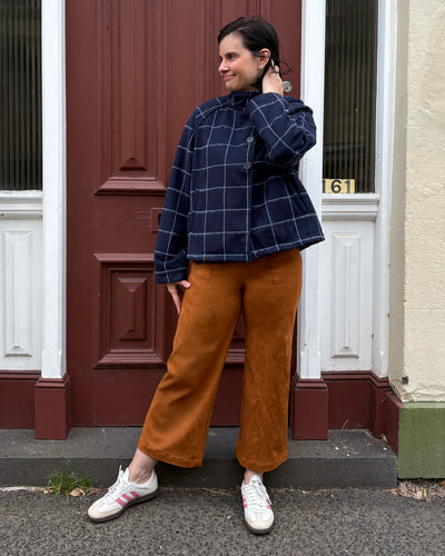 Person wearing a navy checkered jacket and brown suede pants standing in front of a door.