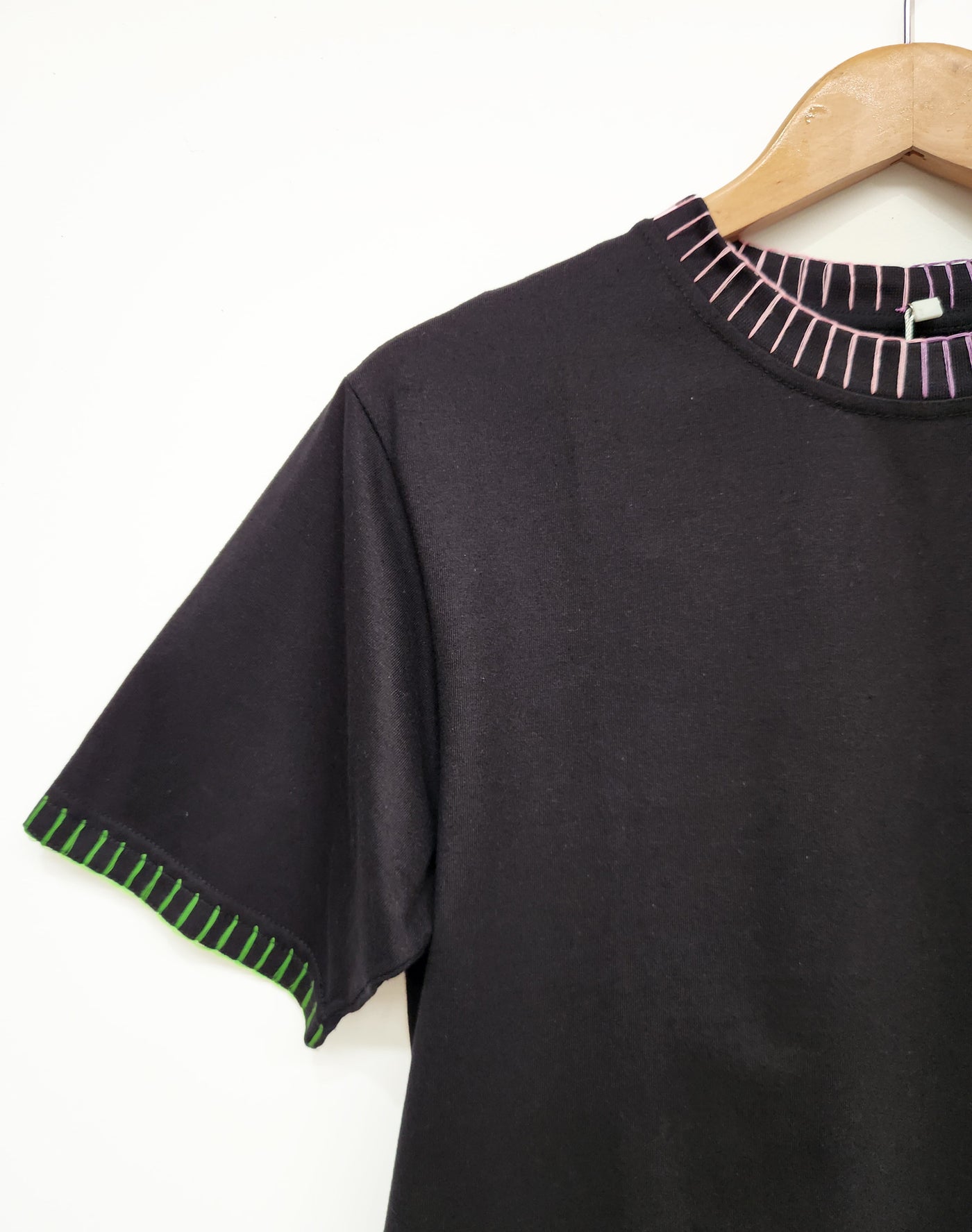 Black t-shirt with green trim on sleeves and collar, hanging on a wooden hanger against a white background.